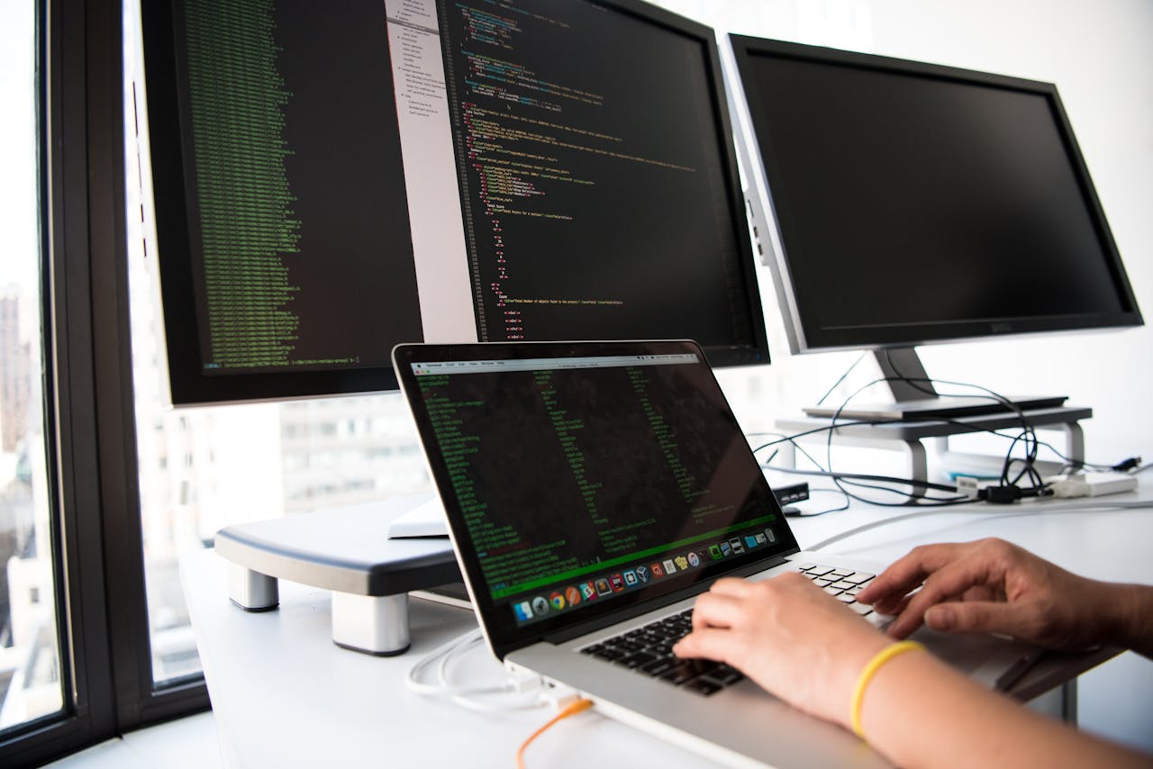 gallery-1 A developer writes code on a laptop in front of multiple monitors in an office setting.