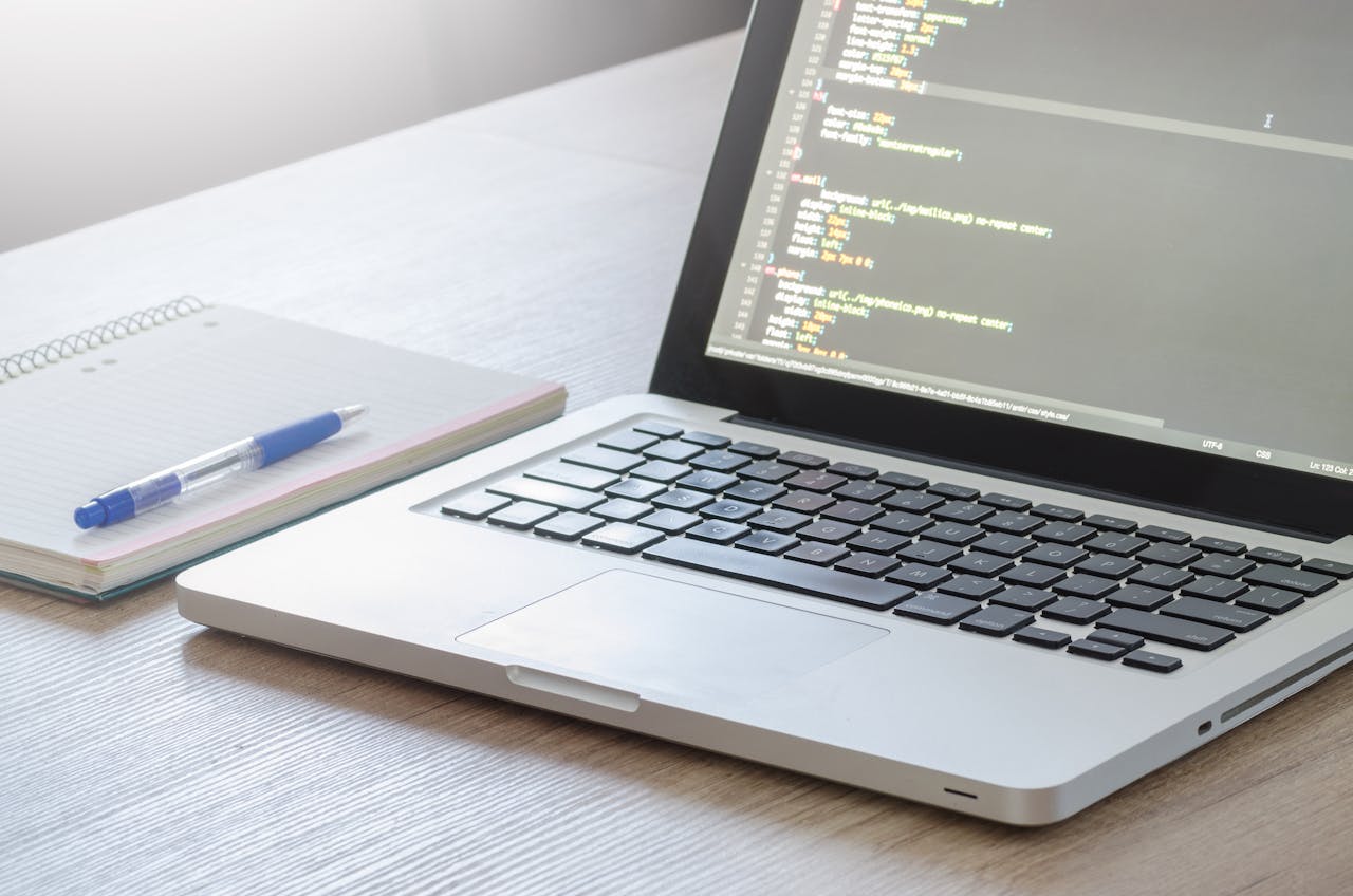 why-choose-us Laptop with code editor open, notebook and pen on wooden desk, perfect for tech and work themes.